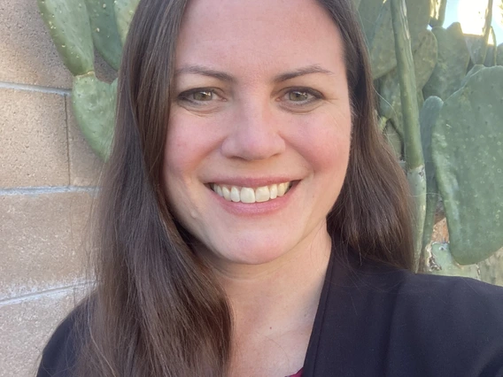 Kelley Merriam-Castro wears a blazer and blouse, smiling in front of a nopal cactus.