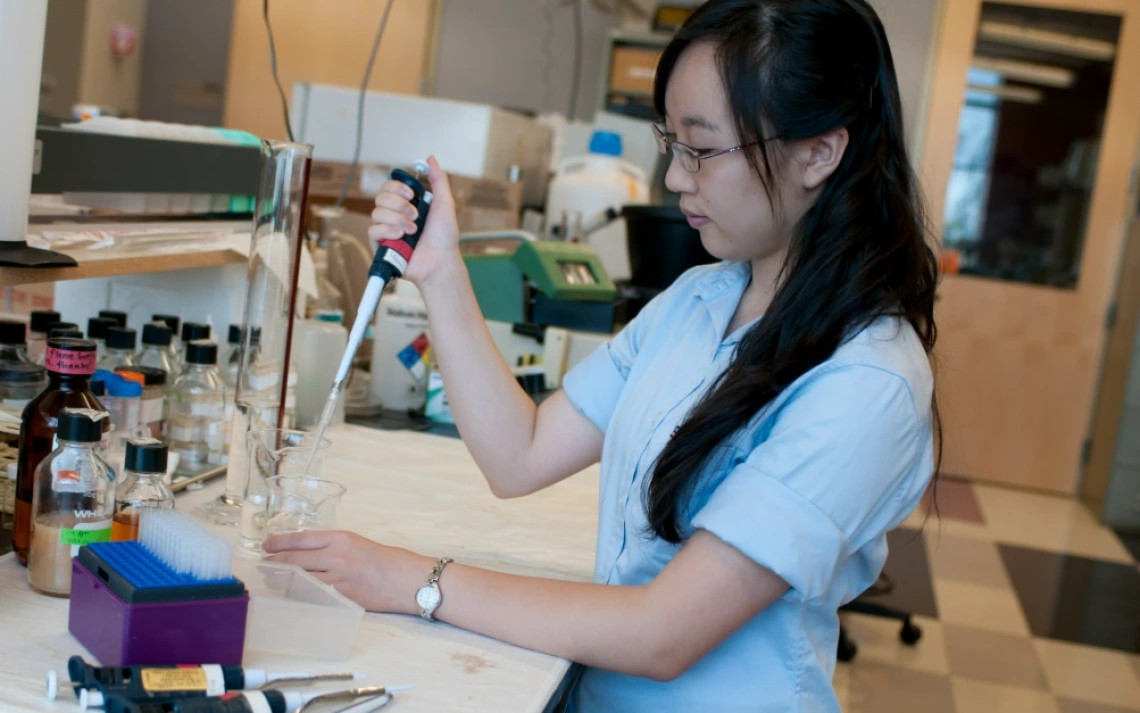 An undergraduate researcher holding an instrument measuring a substance in a beaker